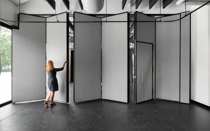 An operable wall part way across a room, panels angled open and one being walked across by hand