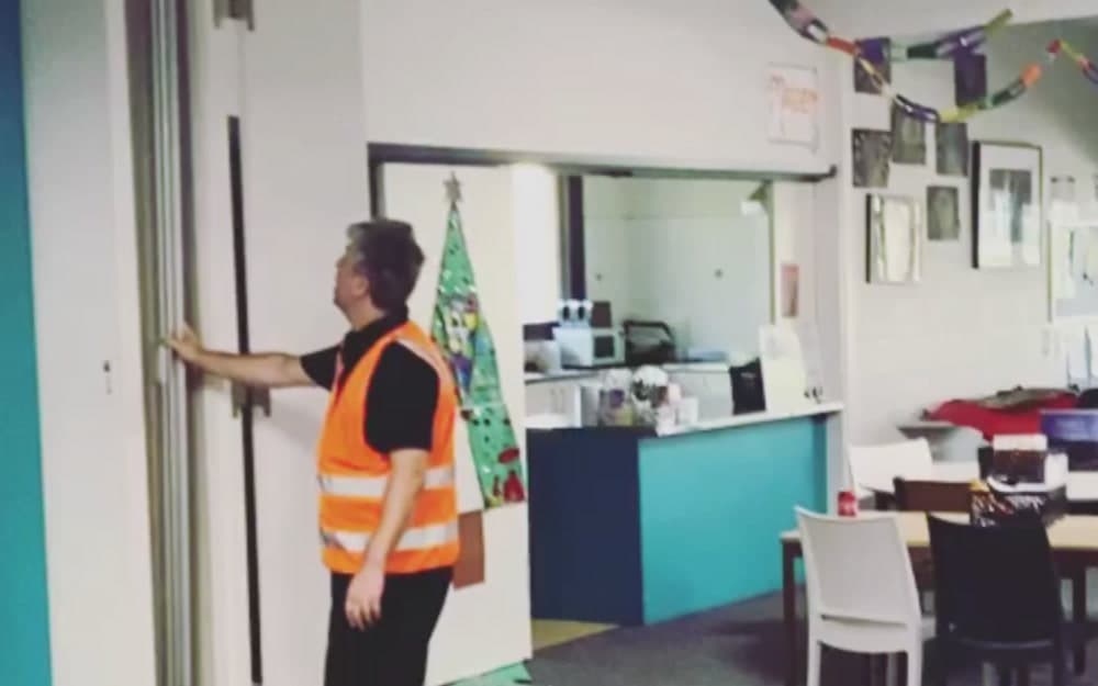 An installer in hi-vis drawing a folding door across an opening in a community hall