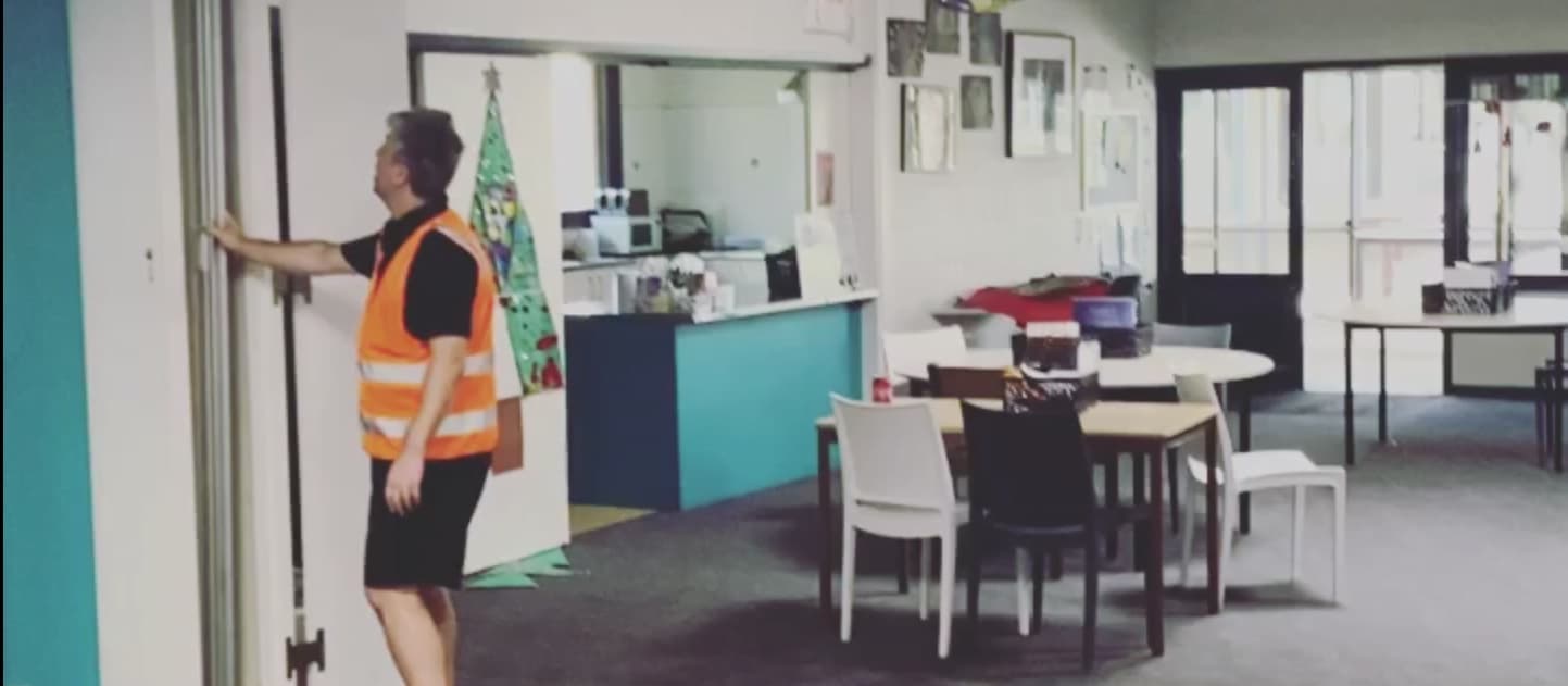 An installer with a hand on a white accordion door, folding it back against the jamb of a community room