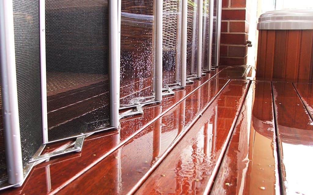 The base of clear folding panels on a wet timber deck, with an insect mesh screen behind them