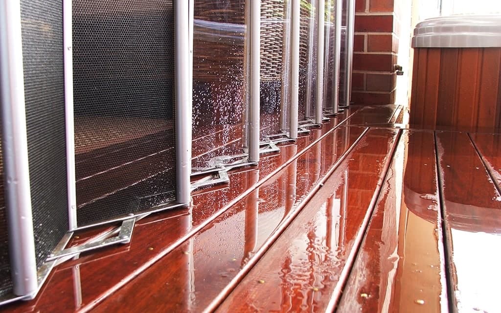 The base of clear folding panels on a wet timber deck, with an insect mesh screen behind them