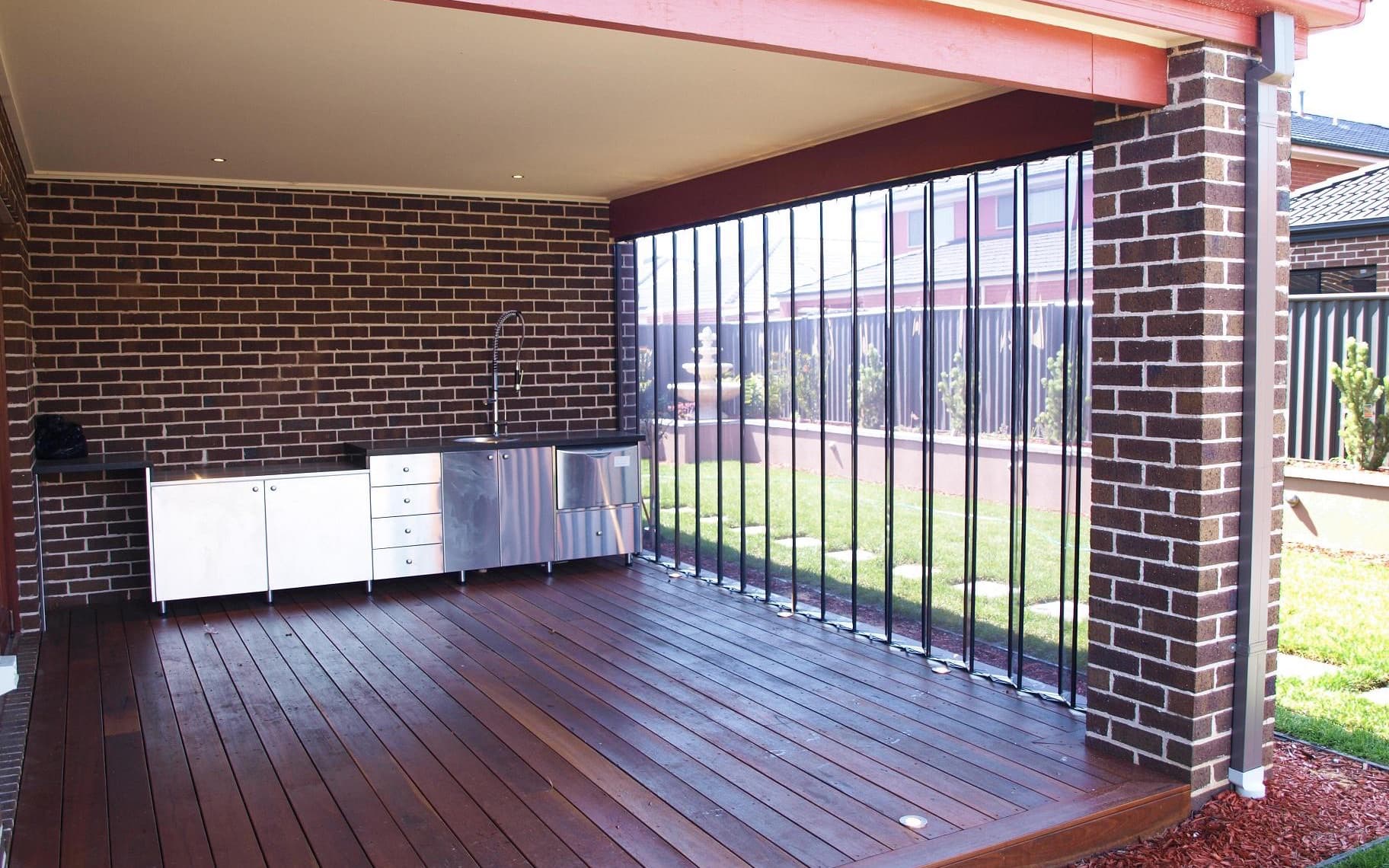 The same alfresco area with the blinds folded back against the pier, the deck and outdoor kitchen open to the lawn