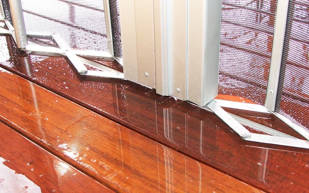 Bottom pivots and guides of clear outdoor blind panels, beaded with rain on a timber deck